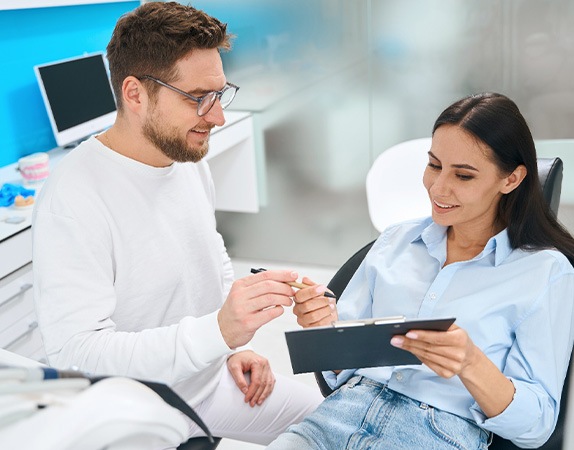 Man in white handing paperwork to patient in dental chair