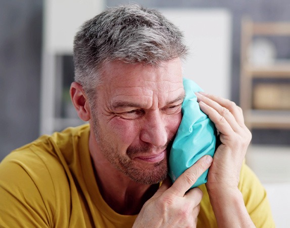 A man applying a compress to his face after dental implant surgery