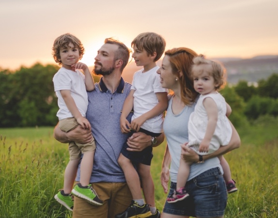 Family of five standing in grass field at sunset