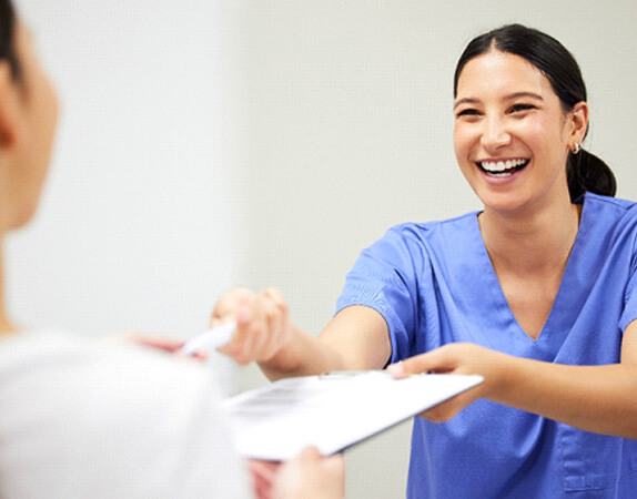 Medical staff in blue scrubs handing paperwork on a clipboard to patient