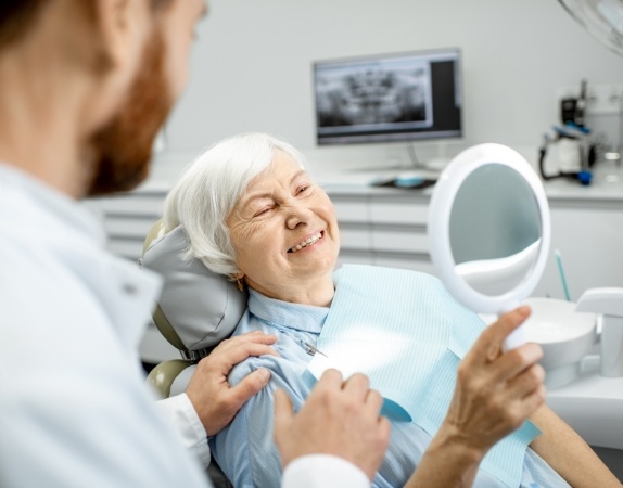 Senior woman in dental chair admiring her smile in mirror