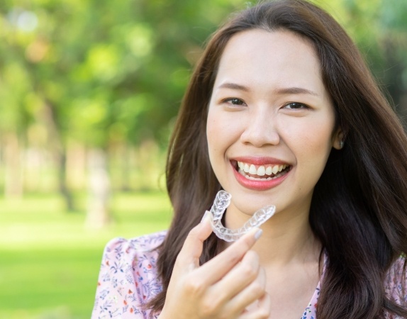 Smiling woman holding an Invisalign tray outdoors