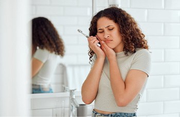 Woman rubbing her toothache after brushing her teeth