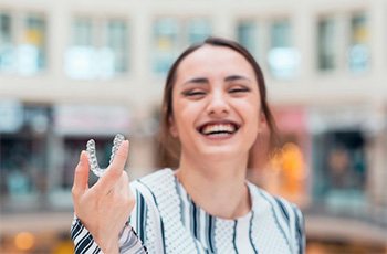 Woman holding an Invisalign tray and smiling