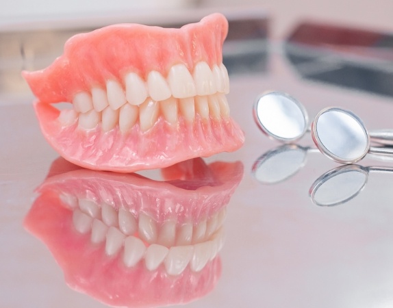 Full dentures on a table next to two dental mirrors