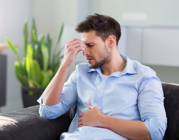 Man sitting on couch and pinching the bridge of his nose