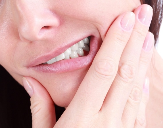 Close up of a person wincing and touching their cheek in pain