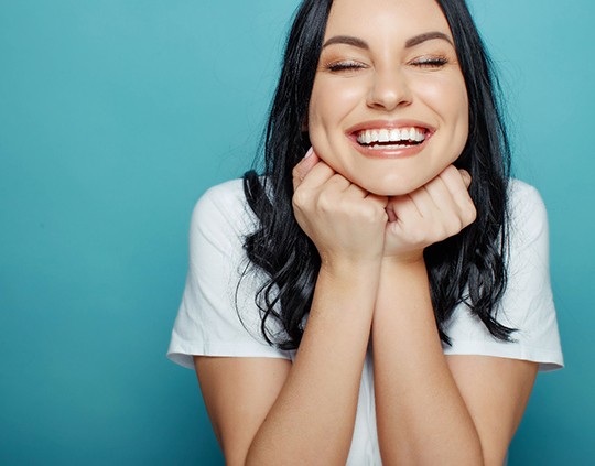 Woman with eyes closed smiling with fists under chin
