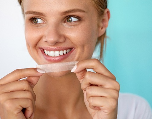 Smiling woman about to apply teeth whitening strip