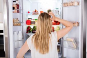 a person scratching their head while looking in a refrigerator