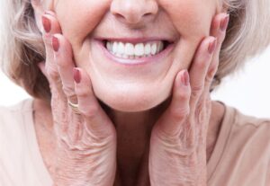 Nose-to-neck view of older woman placing both hands to her cheeks smiling